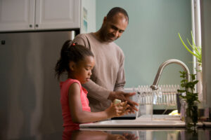 A dad helps his daughter wash her hands at the kitchen sink