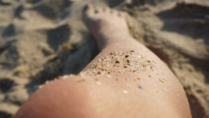 A close-up of a woman's leg with speckles of sand, on the beach
